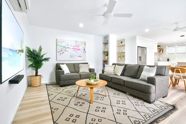 A modern living room with two grey sofas, a coffee table, a large abstract painting, and a potted plant.
