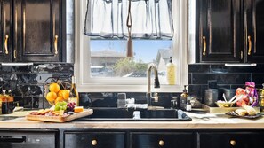 A kitchen with black cabinets, a window with a view of houses, a sink, and various kitchen items.