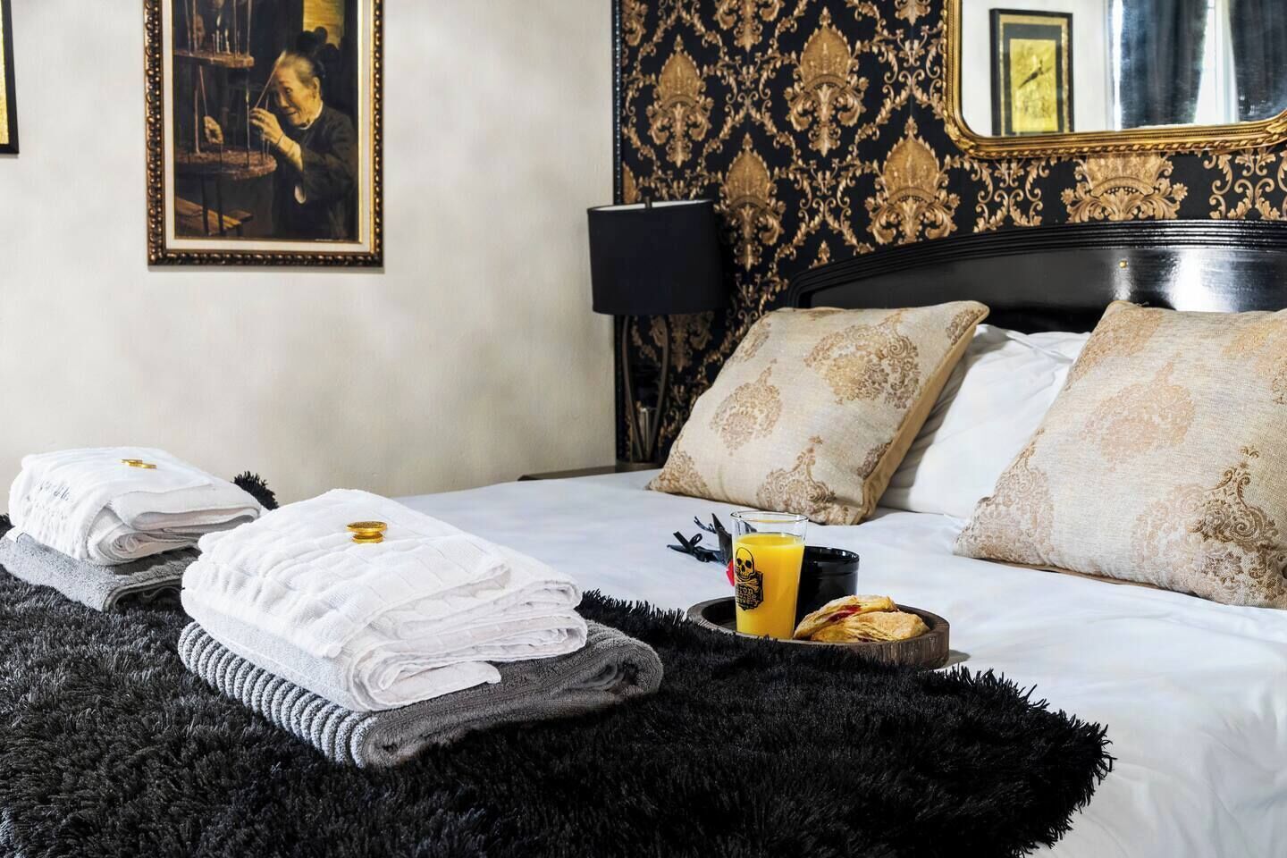 A hotel room with a bed, towels, a tray with breakfast items, a painting, and a mirror.