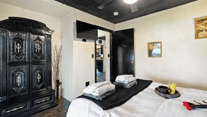 A hotel room with a large black wardrobe, a bed with neatly folded towels, a tray with a cup and orange juice, and a painting on the wall. - THE ONYX — A GOTHIC WINE-COUNTRY HOME WITH A HOT TUB, FIRE PIT AND GAME ROO... (College Place)