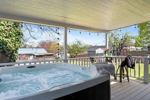Un bain à remous sur une terrasse en bois, avec vue sur un jardin et des maisons.