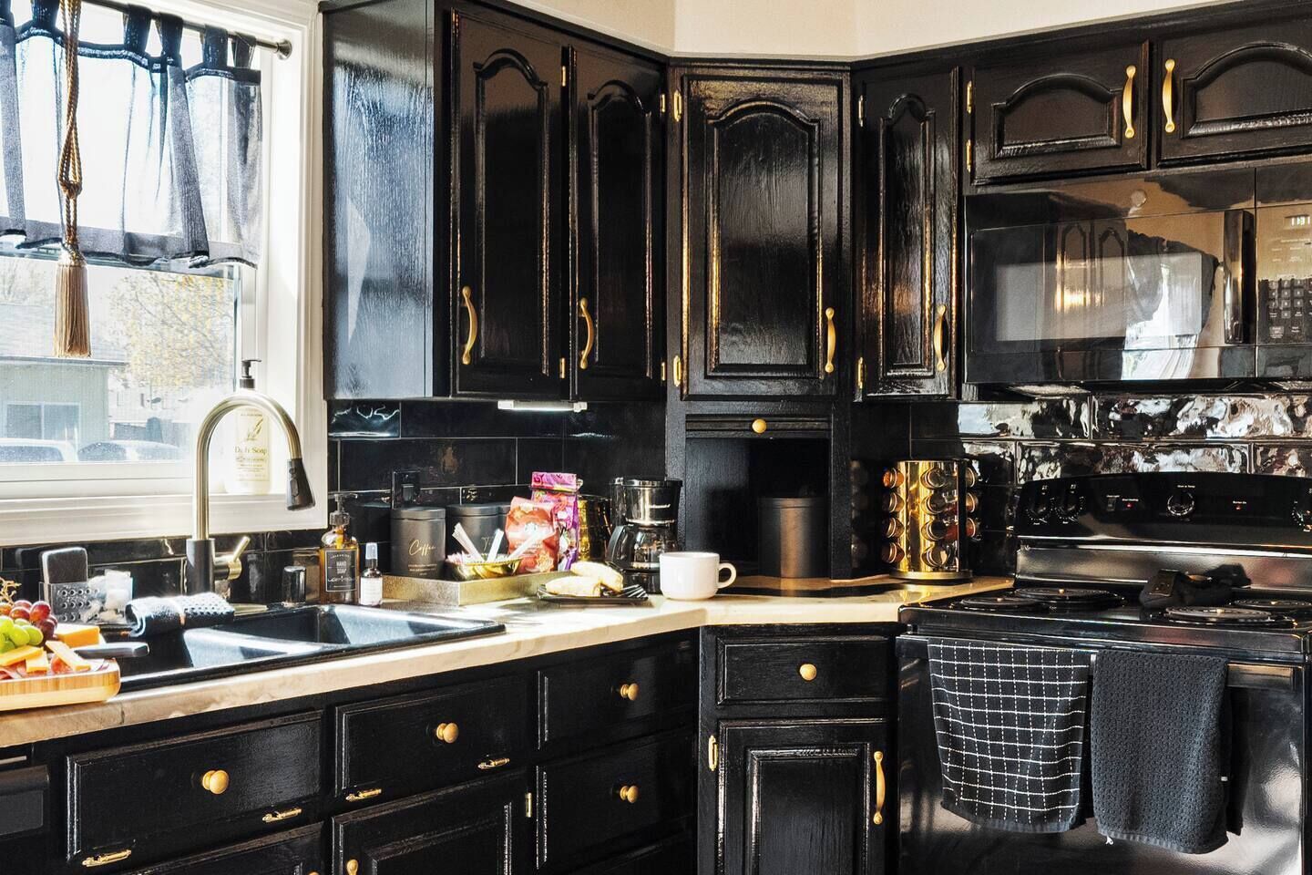 A kitchen with black cabinets, a stainless steel sink, and a coffee machine.