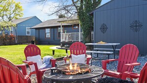 En baghave med et bålsted, røde Adirondack-stole, et picnicbord og et hus med en veranda.
