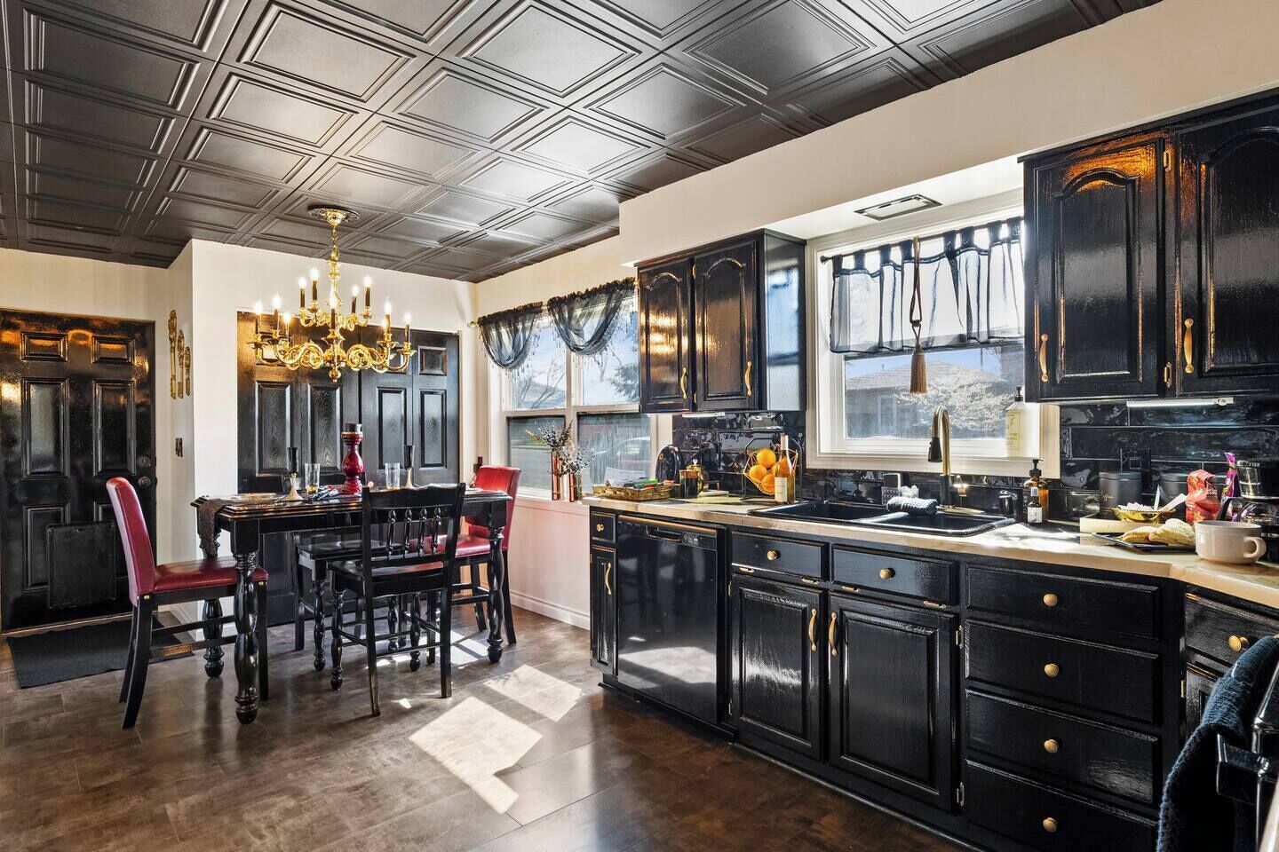 A kitchen with dark cabinetry, a chandelier, and a dining area with red chairs.
