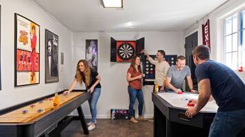 A room with a foosball table, dartboard, and a pool table.