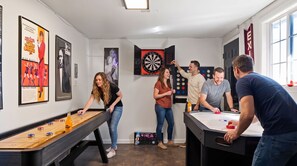 A room with a foosball table, dartboard, and a pool table.