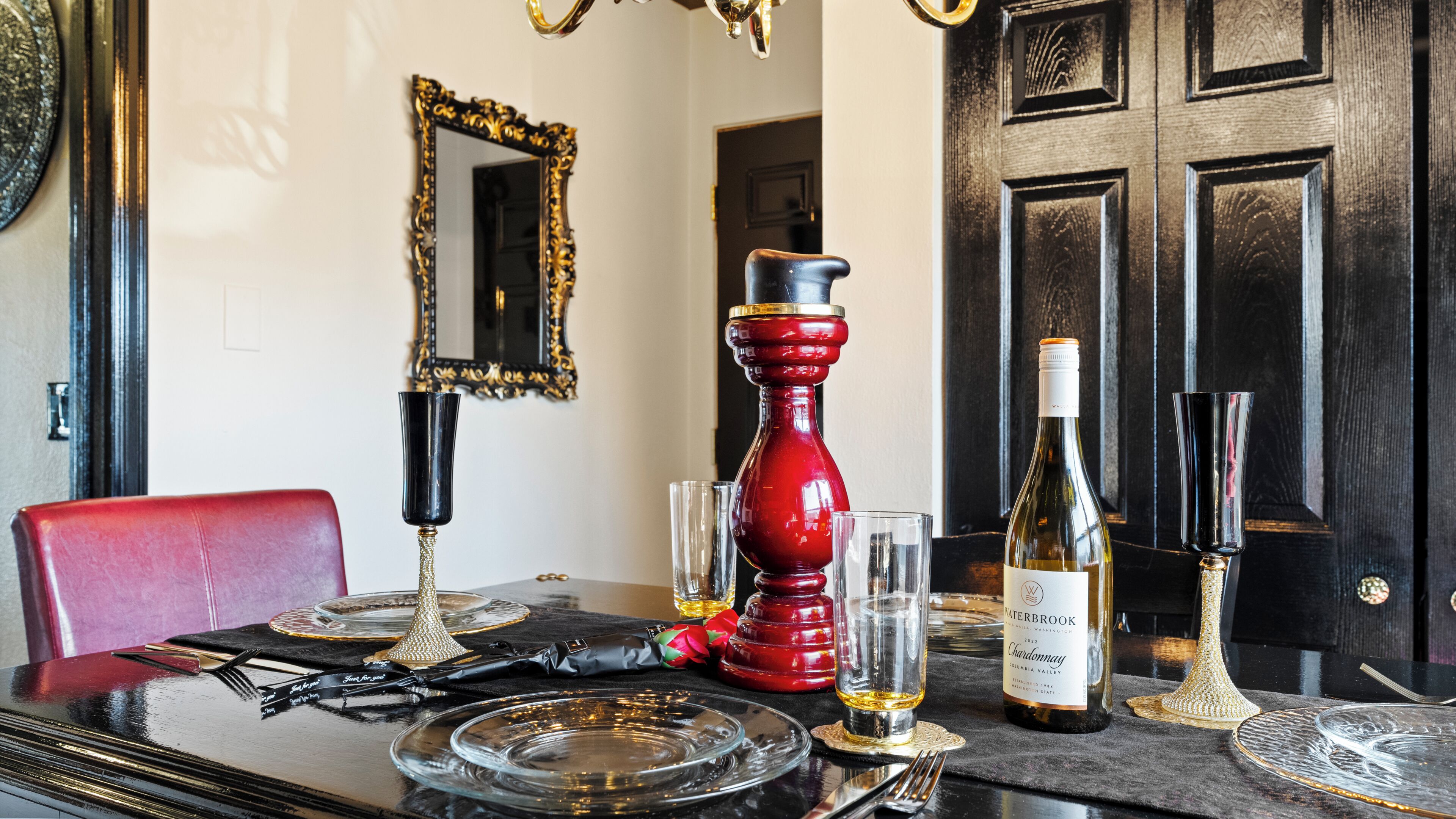 A dining table set with a wine bottle, glasses, and a red candle holder.