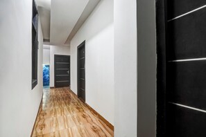 Ein Korridor mit Holzboden und weißen Wänden, der zu einer schwarzen Tür führt.