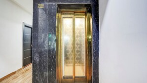 Een lift met een bordje voor de derde verdieping, een deur met een geometrisch patroon, en een muur met een marmerachtige textuur.