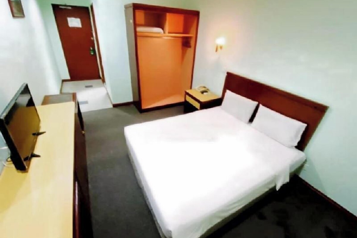 A hotel room with a bed, a desk, a wardrobe, and a bedside table with a lamp.