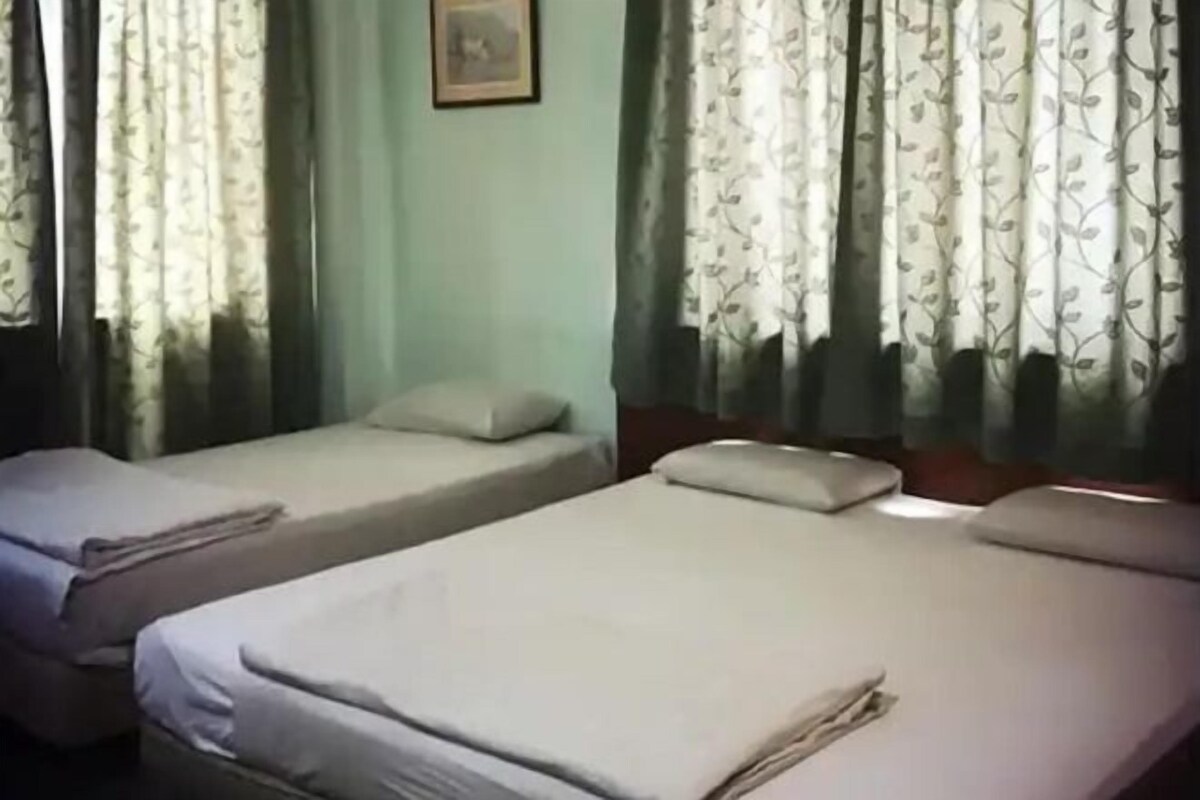 Una habitación con dos camas individuales, un cabecero de madera y un ventanal con cortinas florales.
