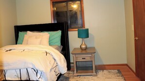 Un dormitorio con cama, mesita de noche, lámpara, ventana y puerta.