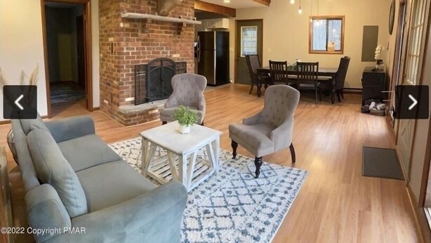 Amplia sala de estar con chimenea de ladrillo, dos sillones, un sofá y un comedor con mesa y sillas.