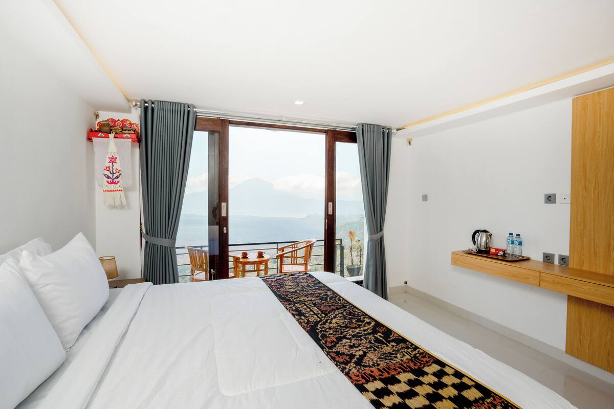 Ein Hotelzimmer mit einem großen Bett, einem Balkon mit Tisch und Stühlen, Bergblick und einem Holzregal mit Gegenständen.