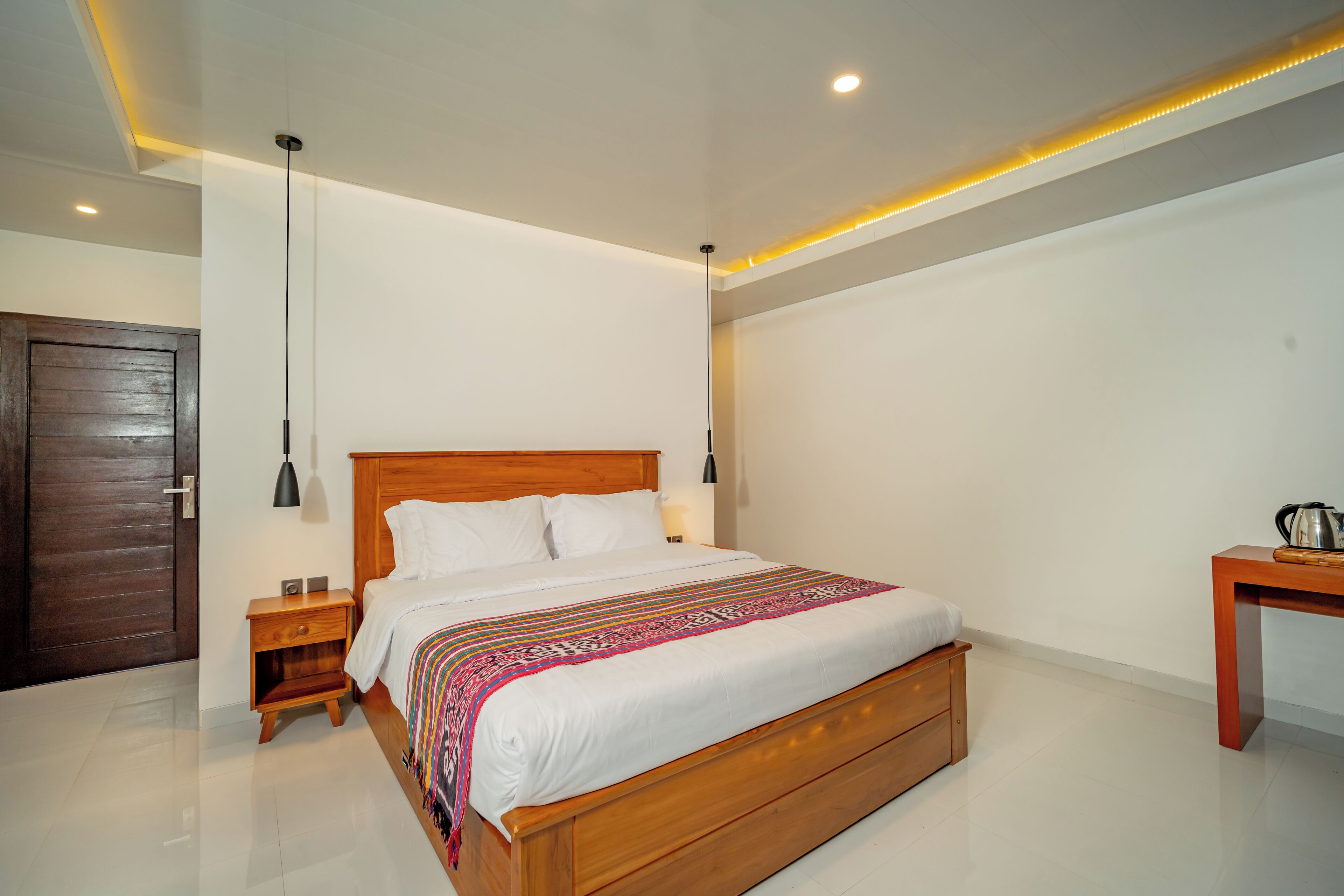 A modern bedroom with a wooden bed, bedside tables, a nightstand, a desk, and a door.