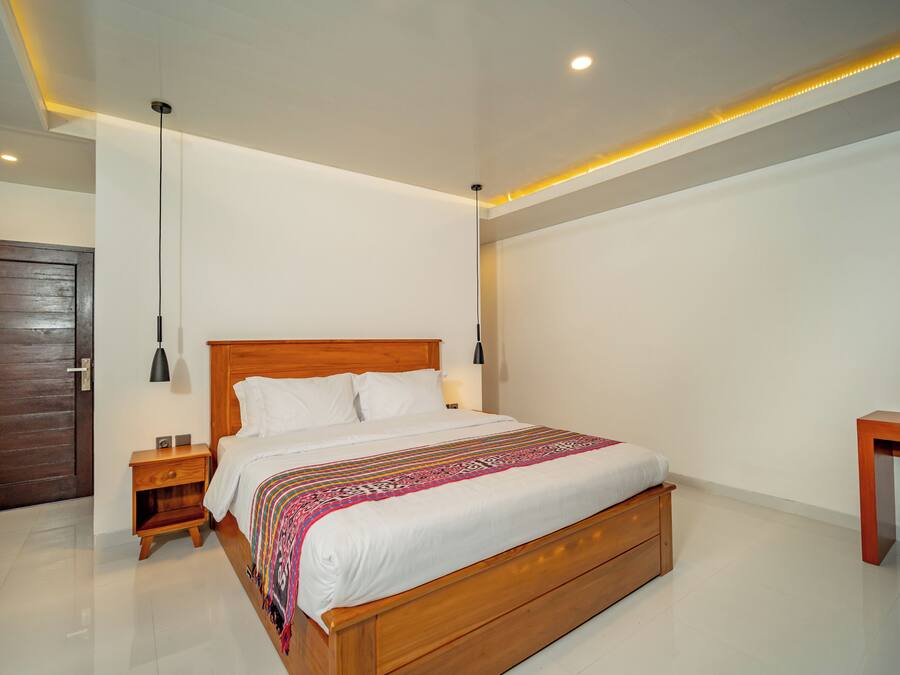 A modern bedroom with a wooden bed, bedside tables, a nightstand, a desk, and a door.
