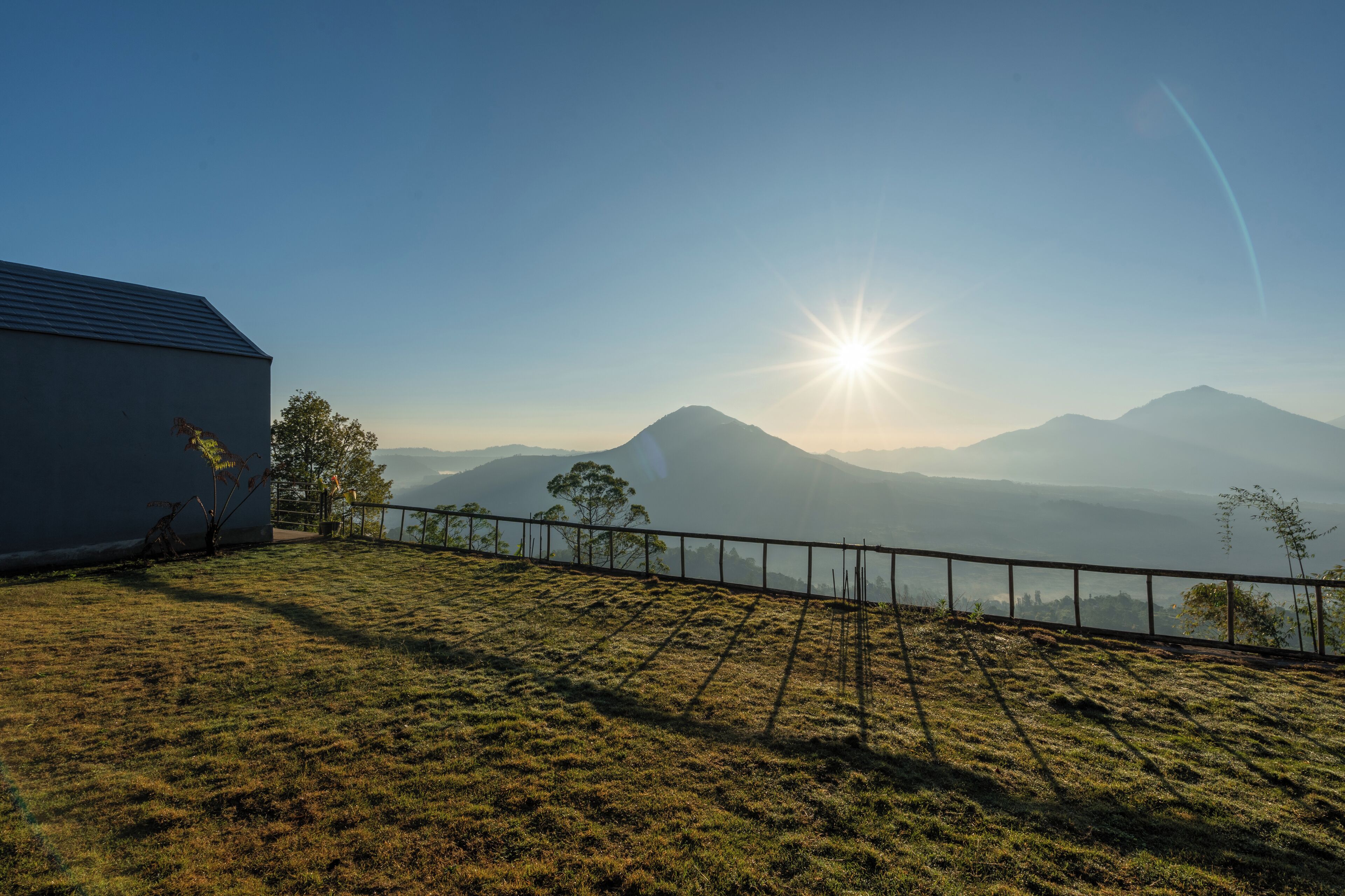 A grassy area with a metal fence, a building, and a mountain range in the background.