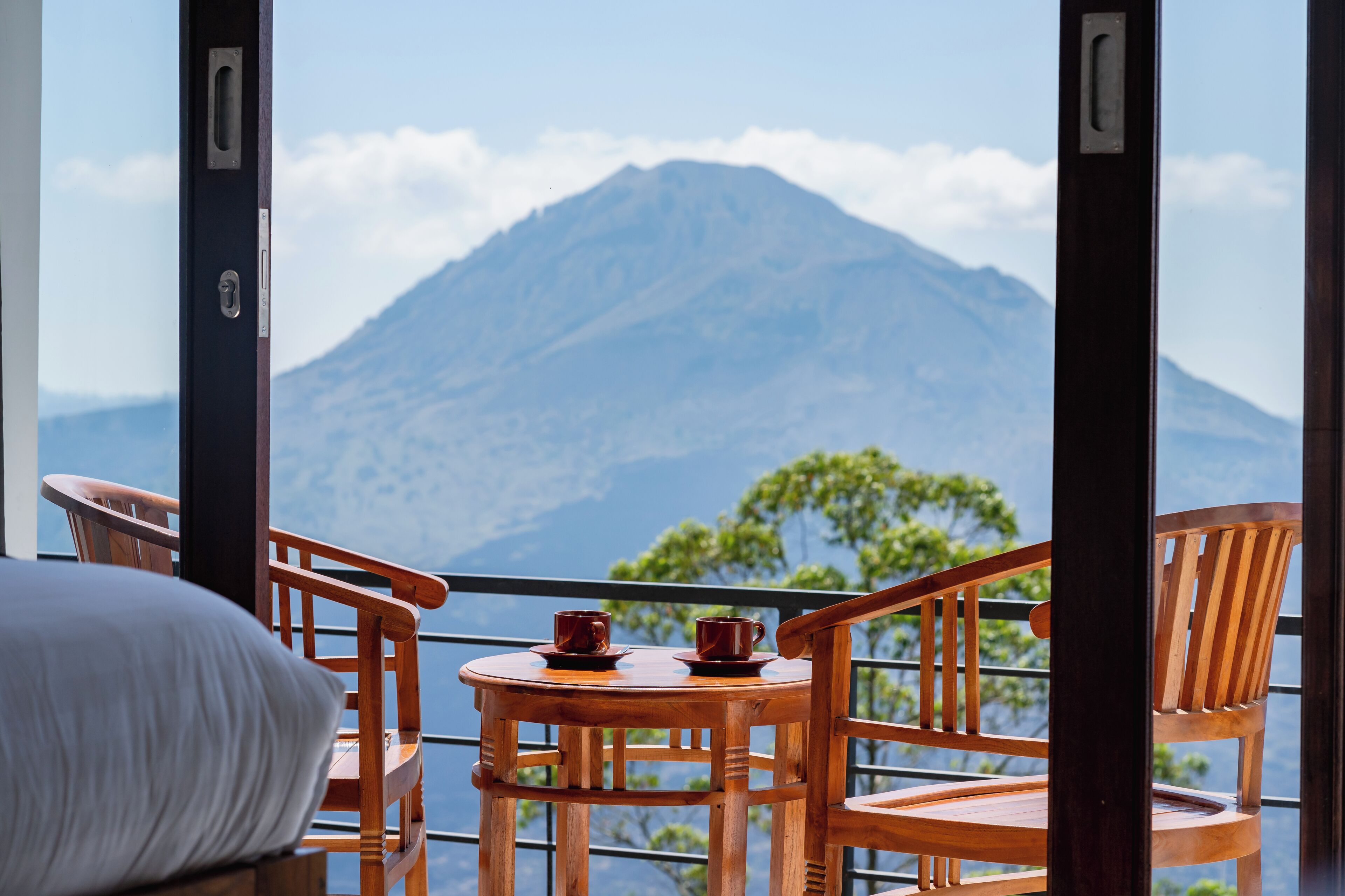 Un balcón con sillas de madera y una mesita, con vistas a una montaña.