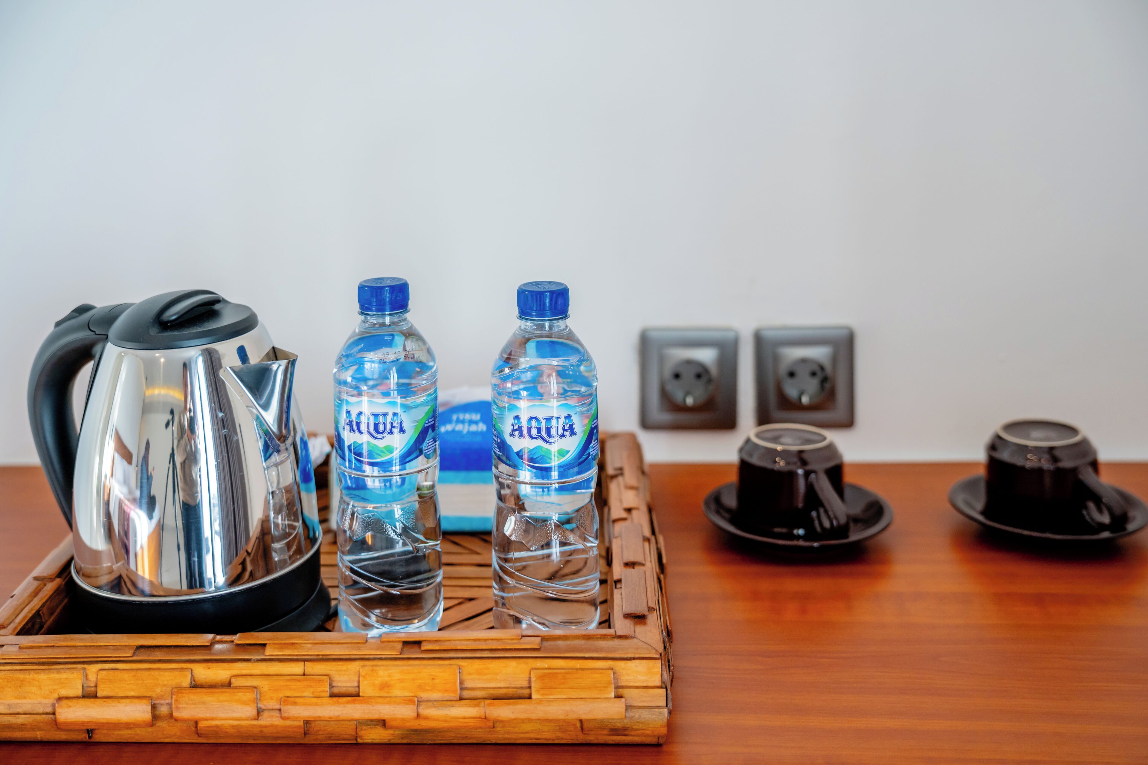 A tray with a kettle, two water bottles, and two cups on a wooden table.