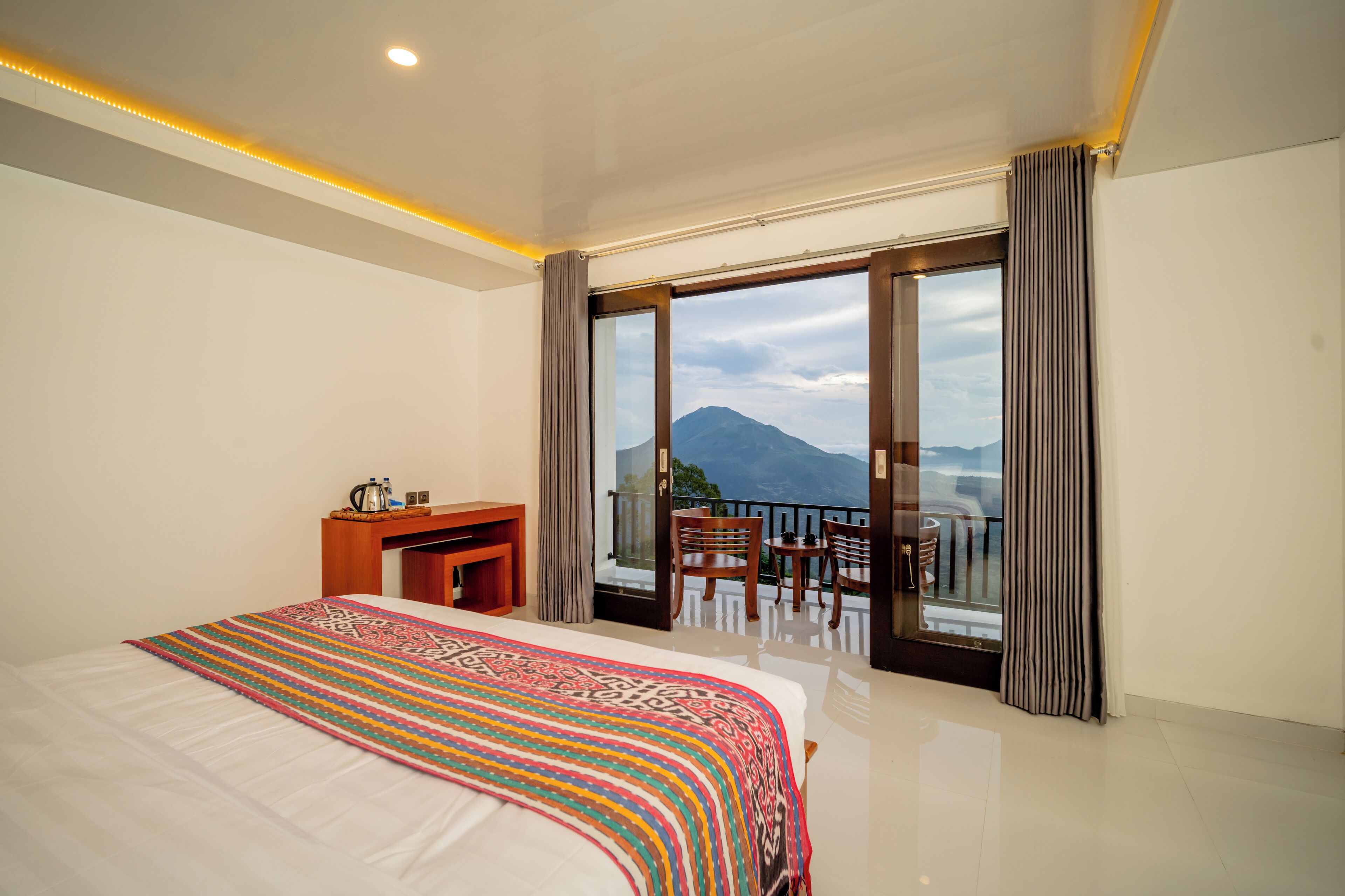 A hotel room with a large bed, a desk, and a balcony with a view of a mountain.