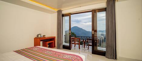 A hotel room with a large bed, a desk, and a balcony with a view of a mountain.