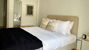 Ein Schlafzimmer mit einem Bett, einem Nachttisch, einem Spiegel und einem an der Wand befestigten Lichtschalter.