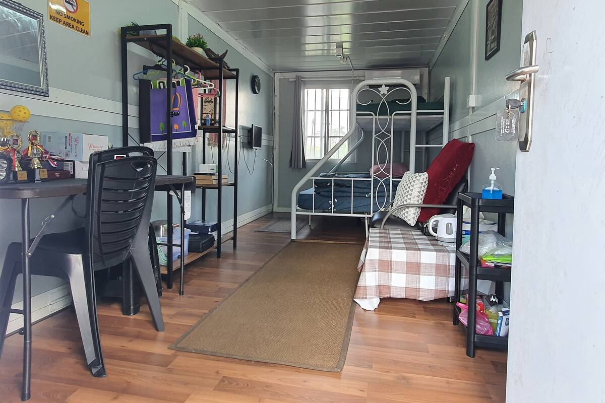 A compact room with a desk, chair, bunk bed, and a small kitchenette area.