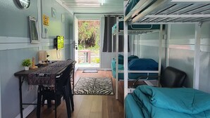 Quarto compacto com beliches, escrivaninha com cadeira, mesinha e relógio na parede.