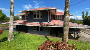 Uma casa de dois andares com telhado de telhas vermelhas, cercada por palmeiras e um gramado.