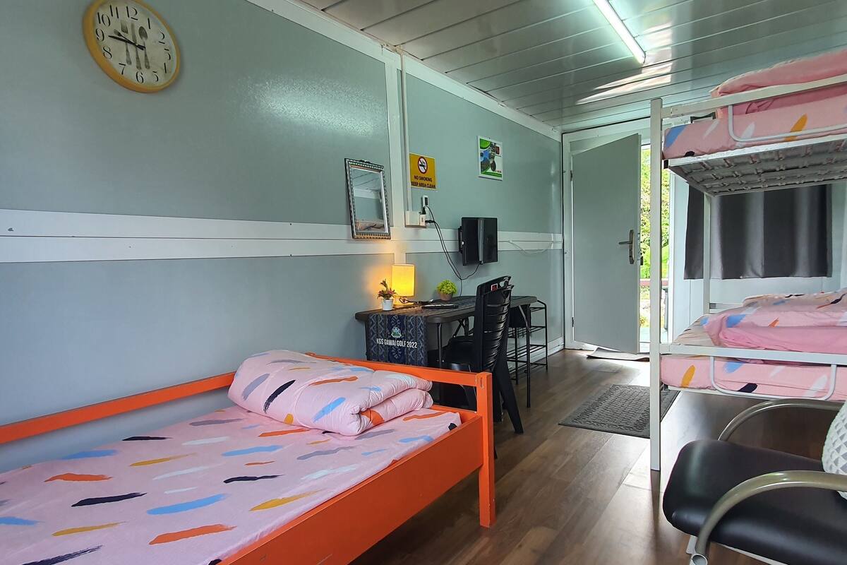 A room with a single bed, a desk with a chair, a television, and a clock on the wall.
