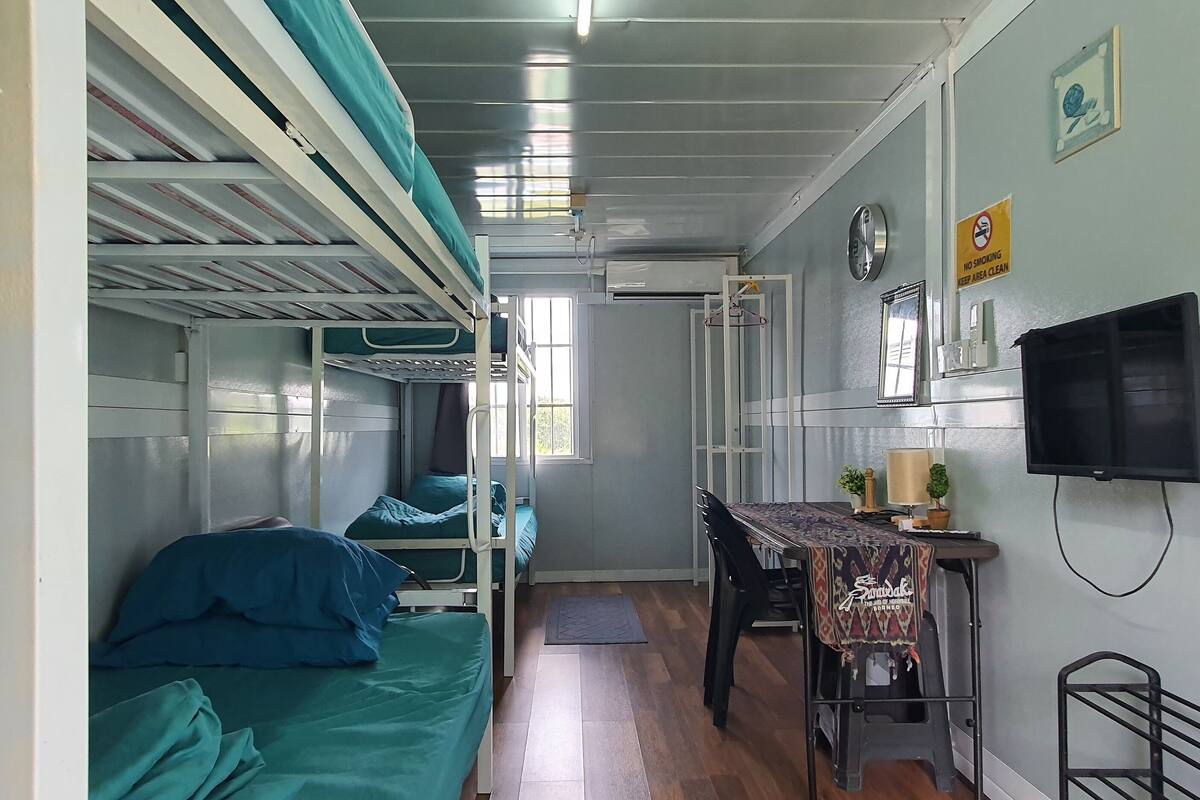 A compact room with bunk beds, a small desk with a chair, a television, and a clock on the wall.