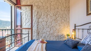 Ein Schlafzimmer mit Stehwand, einem Balkon mit Metallgeländer, einem Bett mit blauer Bettwäsche und einem Nachttisch mit Lampe.