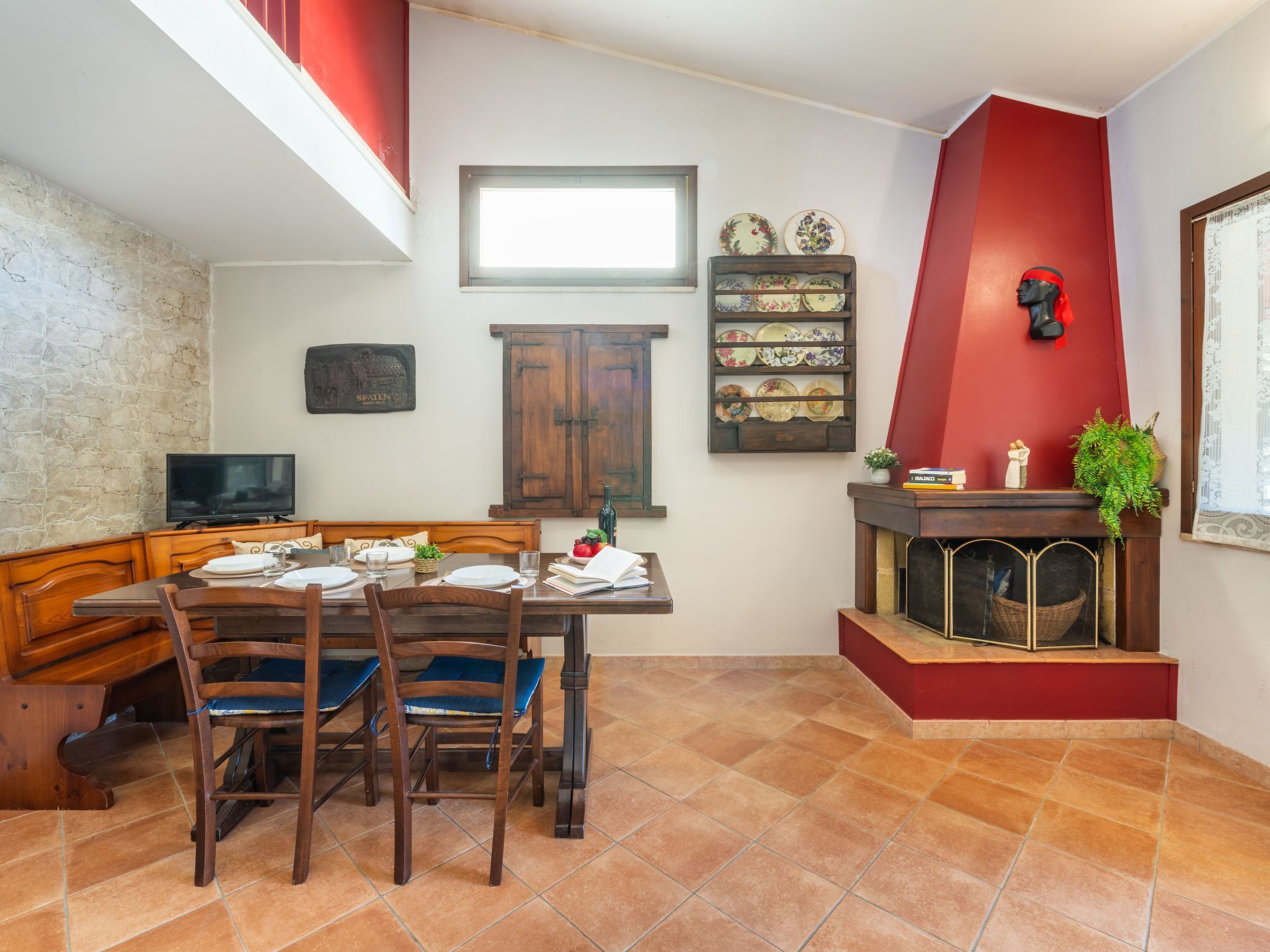 A dining area with a wooden table and chairs, a television, a fireplace, and a red accent wall.