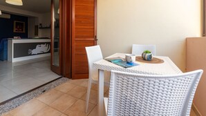 Ein kleiner, gut beleuchteter Raum mit einem weißen Tisch und Stühlen, einer Holztür und einem Blick in einen Wohnbereich mit einer Couch und einem Bild.