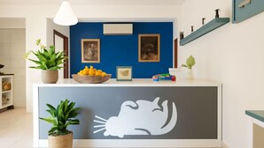 Ein Empfangstresen mit blauer Wand, gerahmten Bildern, einer Zitronenschale und Topfpflanzen.