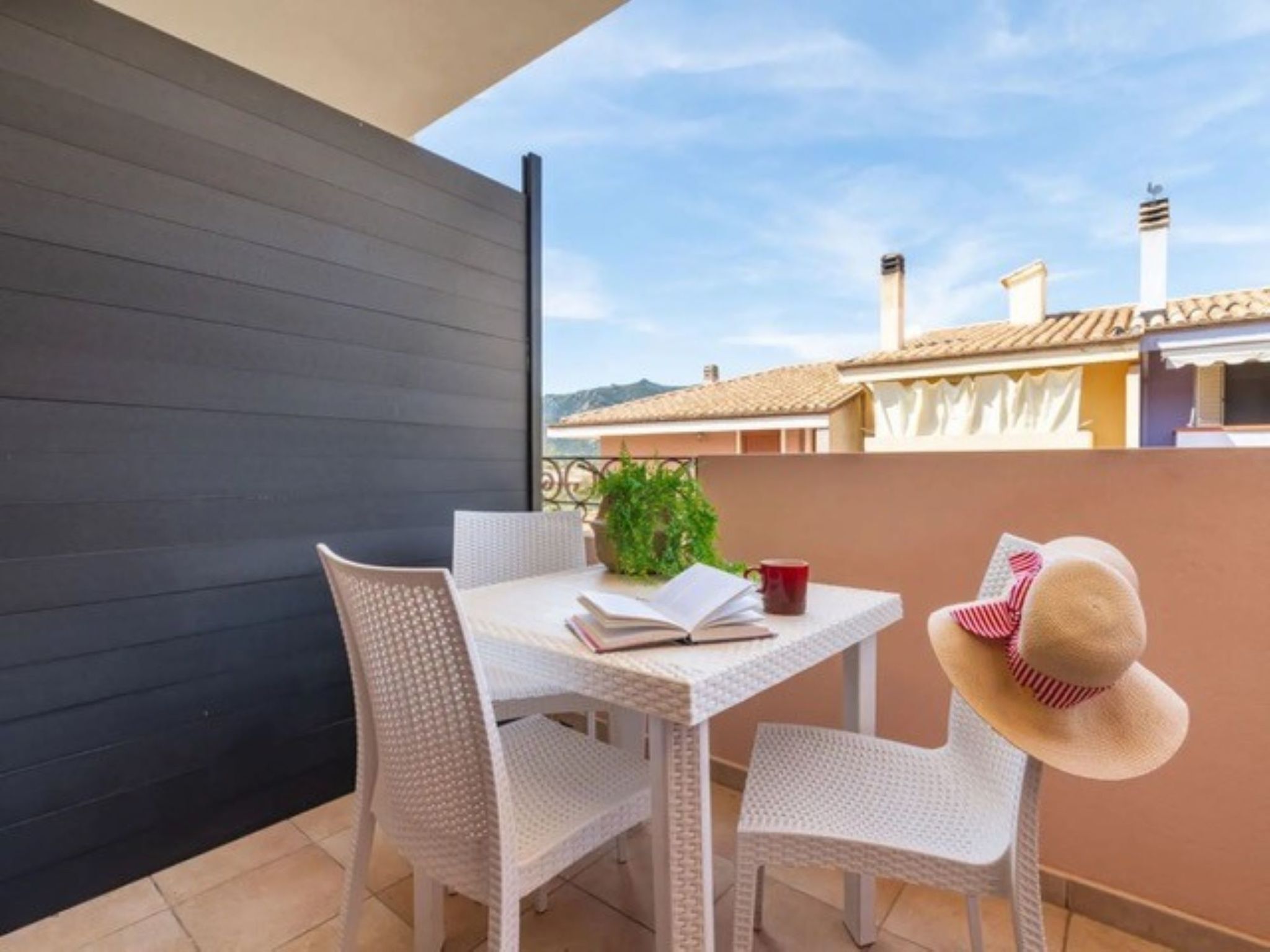 A balcony with a table, chairs, a book, a plant, and a hat.