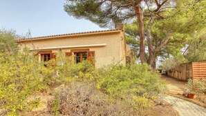 Una casa con techo de tejas, un pequeño jardín delantero con diversos arbustos y una valla de madera.