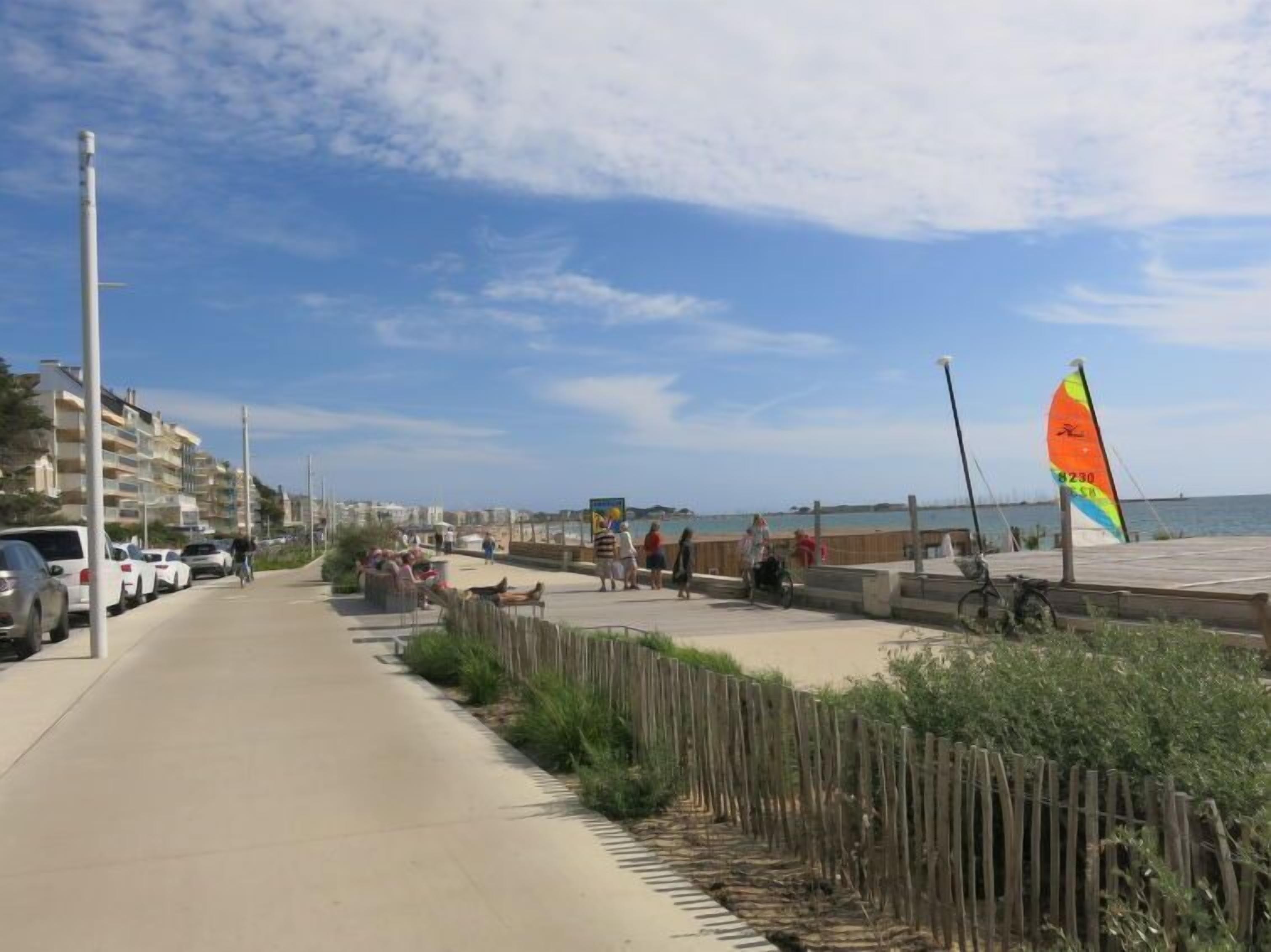 Un passeig marítim amb una tanca de fusta, un veler i un cel serè.