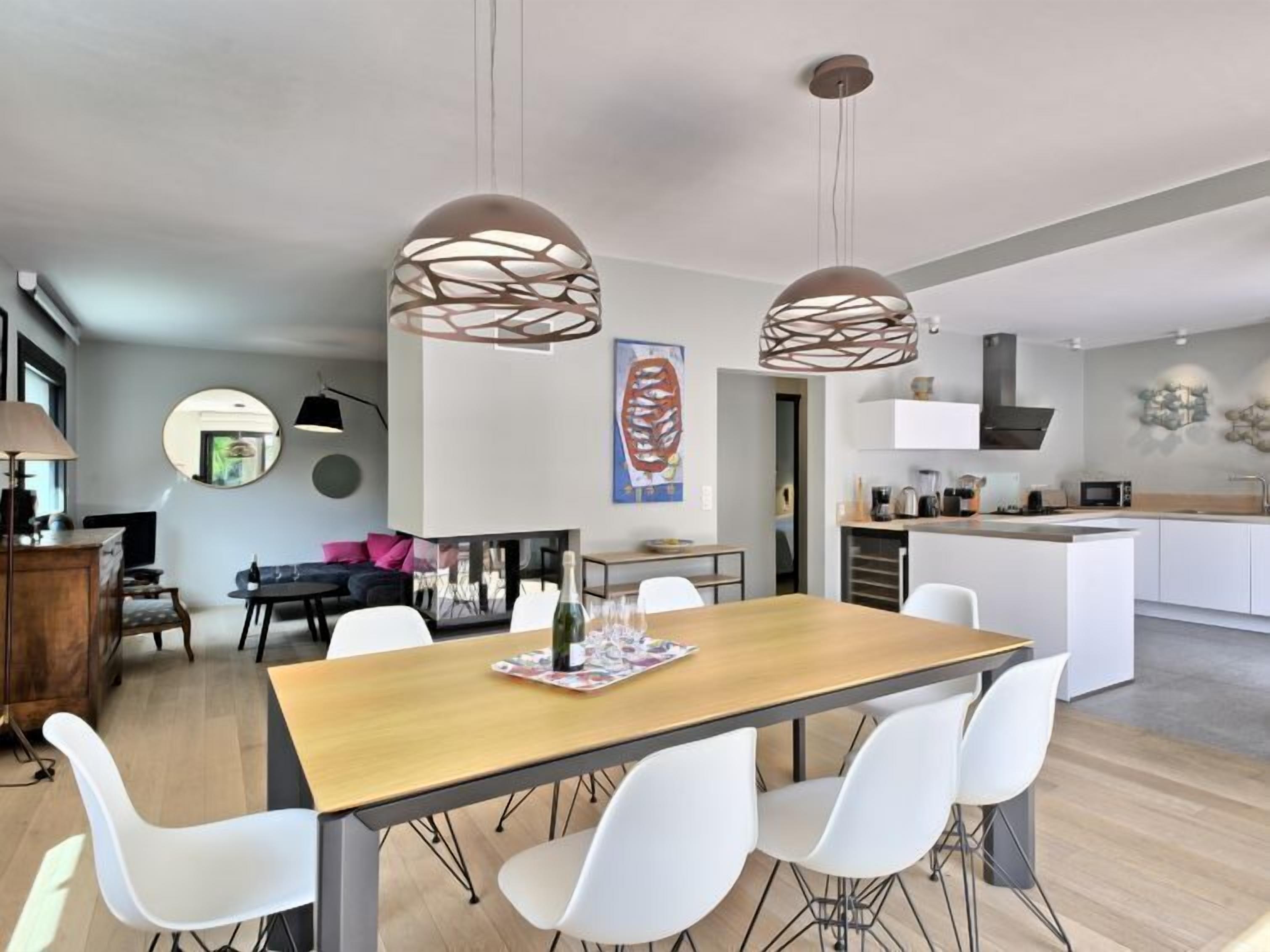 Una cucina moderna con mobili bianchi, un'isola centrale e un'area pranzo con tavolo in legno e sedie bianche.