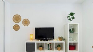 Un salon moderne doté d’un téléviseur à écran plat, d’un meuble de rangement blanc avec des étagères et d’œuvres d’art décoratives accrochées au mur.