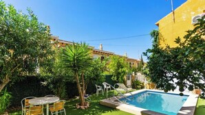 Un jardin avec une piscine, une petite table entourée de chaises et un palmier.