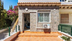Un bâtiment en pierre avec une terrasse carrelée, une fenêtre grillagée et un petit climatiseur.