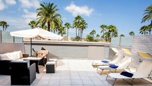 A rooftop terrace with a dining area, lounge chairs, and a view of palm trees and the ocean. - Golden Ray by Interhome (Jávea)