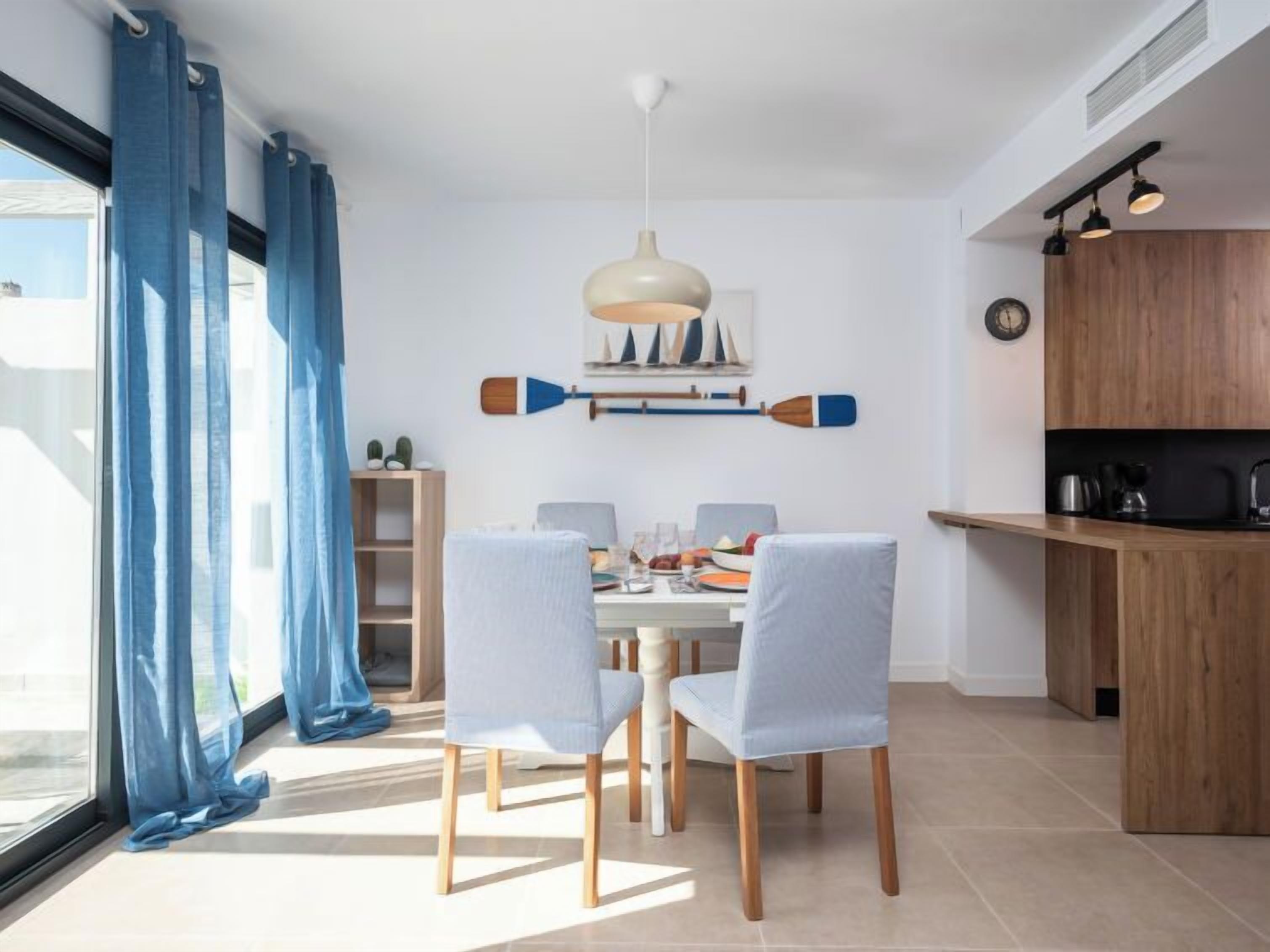 A modern dining area with a white table, four chairs, and a pendant light.