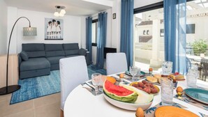 A modern living room with a grey sofa, a white armchair, and a dining table set with fruits and glasses. - Campanario Townhouse by Interhome (Estepona)