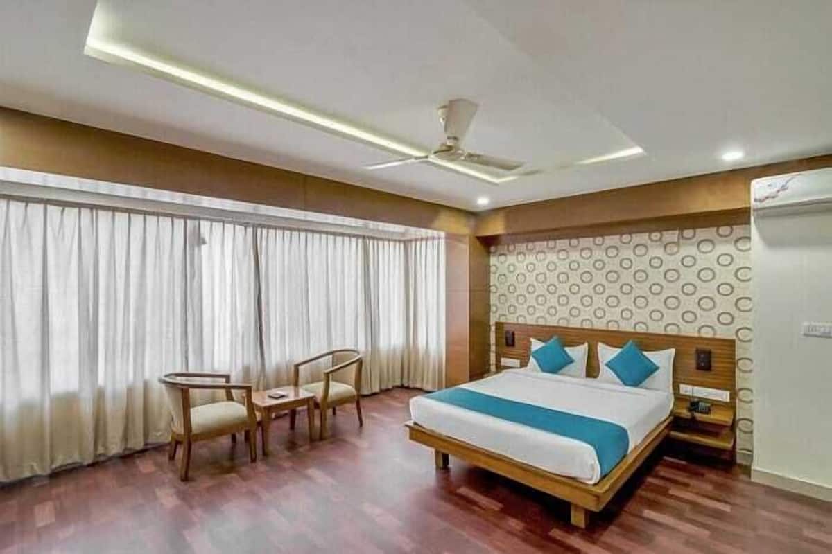 A hotel room with a bed, two chairs, a table, a ceiling fan, and a window with curtains.