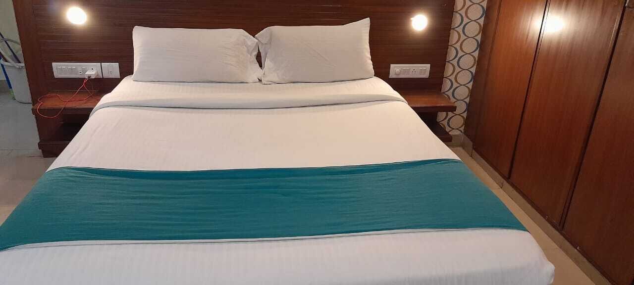 Un lit bien fait, avec une literie blanche et turquoise, une tête de lit en bois et des tables de chevet avec des lampes.