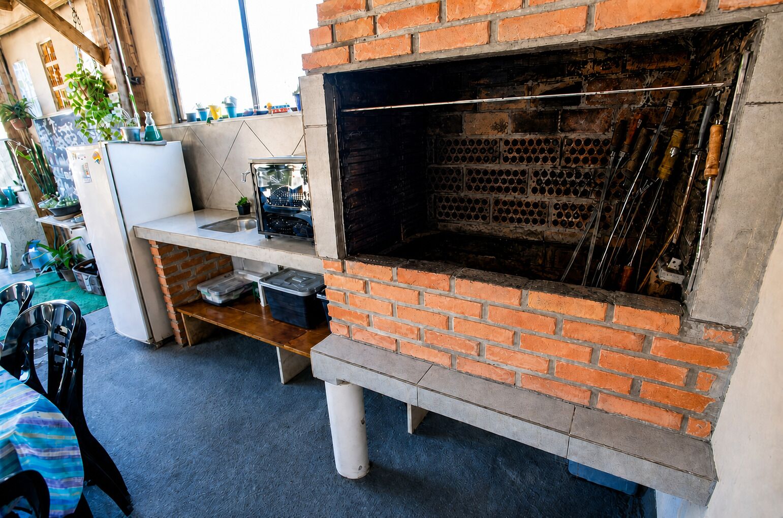 A brick oven with a metal door, a white refrigerator, and a shelf with various items.