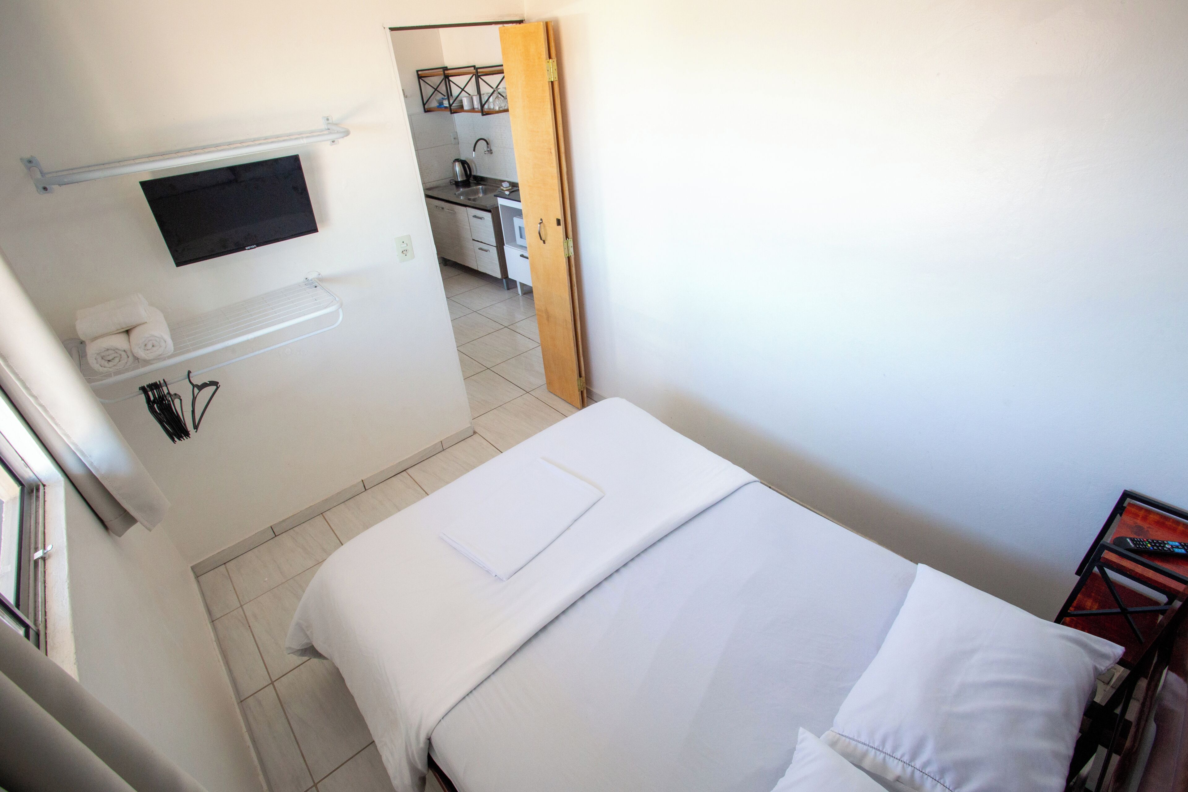 A hotel room with a bed, a TV mounted on the wall, a towel rack, and a small table with a remote control.