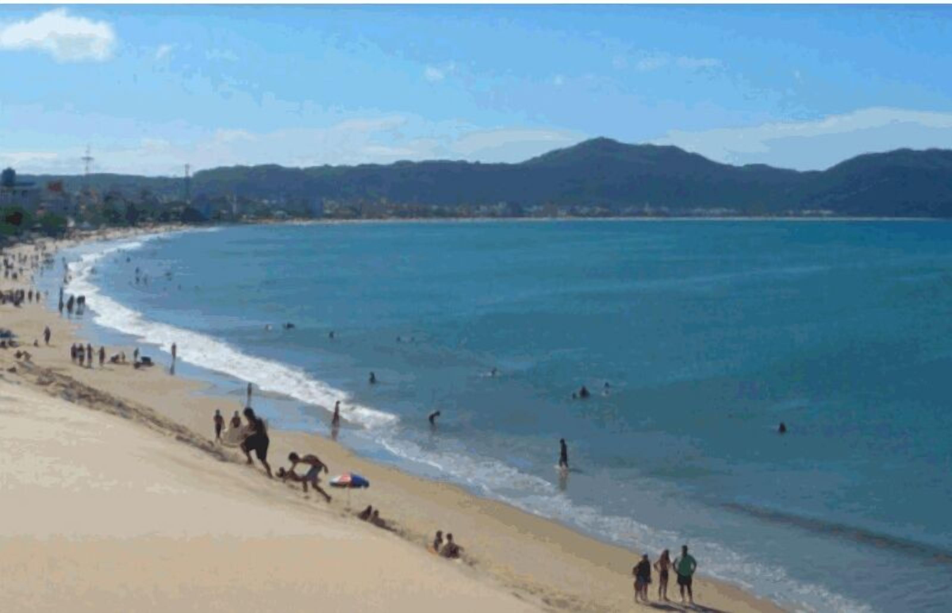 A beach with people swimming and walking along the shore.